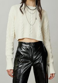 Kerman neulottu cropped-neule, jossa on ribatut hihat, yhdistettynä korkeavyötäröisiin mustiin kiiltävistä keinonahasta valmistettuihin housuihin. Kerrokselliset hopeaketjut.