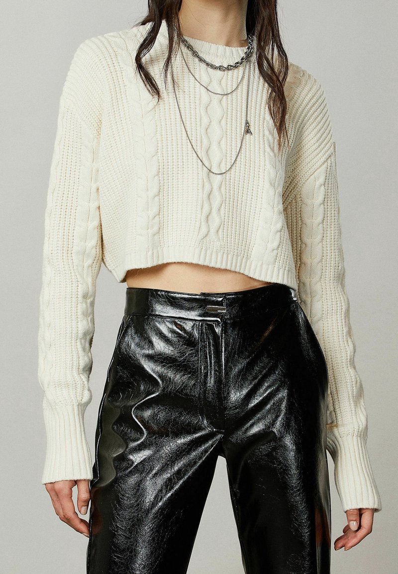 Kerman neulottu cropped-neule, jossa on ribatut hihat, yhdistettynä korkeavyötäröisiin mustiin kiiltävistä keinonahasta valmistettuihin housuihin. Kerrokselliset hopeaketjut.