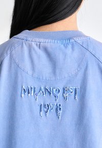 Ljusblå sweatshirt med broderad text "MILANO EST 1978" med dropeffekt, ribbad krage och mjuk tygkvalitet.