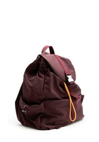 Zaino di tessuto bordeaux con pattina pieghevole, spallacci regolabili e un cordino arancione come accent. Presenta ampi tasconi laterali e un design minimalista.