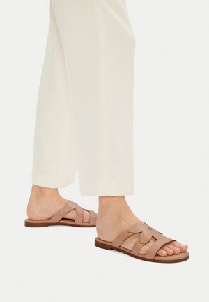 Hellrosa flache Slide-Sandalen mit mehreren Riemen, floralen Akzentdetails und flacher Sohle, kombiniert mit cremefarbenen, weit geschnittenen Hosen.