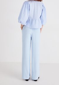 Haut à manches bouffantes en vichy bleu clair avec une taille peplum, associé à un pantalon largement taille haute bleu clair en tissu doux.