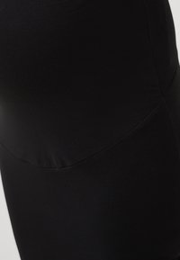 Detailní záběr na černou tkaninu s viditelným švem, ukazující hladký, elastický materiál, který se obepíná kolem tvaru.