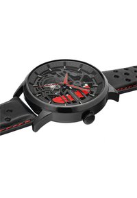 Montre noire avec un cadran transparent, des accents rouges et un bracelet noir texturé. Les caractéristiques incluent des index horaires en gras et une couronne proéminente.