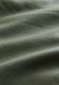 Material de culoare verde măsliniu, cu o textură fină, având ușoare ondulații și un luciu, indicând moliciune și elasticitate.