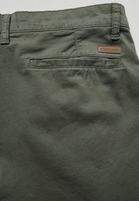 Olivově zelené bavlněné kalhoty s hladkým povrchem, obsahující zadní kapsu a hnědou koženou nášivku nad pravou kapsou.