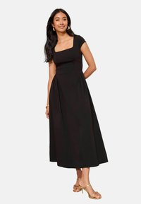 Must pikk kleit ruudukujulise kaelusega, lühikeste varrukatega ja voltidega külgedel. Modell kannab kuldseid kontsaga sandaale ja rõngaskujulisi kõrvarõngaid.