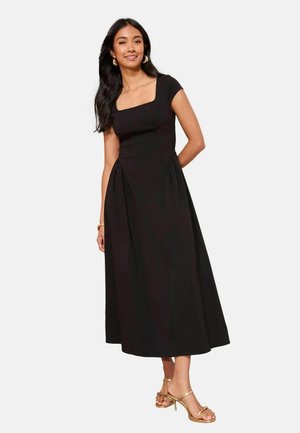 Must pikk kleit ruudukujulise kaelusega, lühikeste varrukatega ja voltidega külgedel. Modell kannab kuldseid kontsaga sandaale ja rõngaskujulisi kõrvarõngaid.