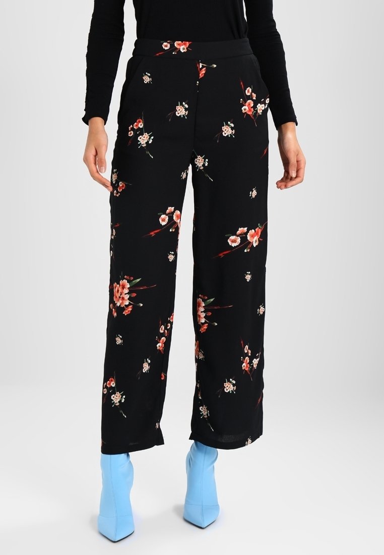 Pantalons floraux noirs à coupe ample, ornés d'un mélange de petites fleurs rouges et blanches. Taille élastique et poches latérales.