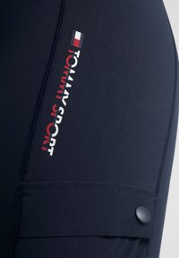 Granatowe spodenki sportowe z logo "TOMMY SPORT" w czerwonym i białym kolorze. Posiadają boczną kieszeń oraz gładki, elastyczny materiał.