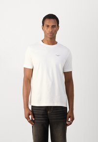 Witte katoenen t-shirt met korte mouwen en ronde hals, met een klein gedrukt logo op de borst. Gekoeld met donkere denimmicro.
