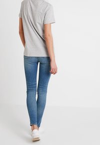 Camiseta de manga corta gris combinada con unos vaqueros ajustados de color azul desgastado. Los vaqueros presentan un ligero patrón de desgaste, y lleva zapatillas blancas en los pies.