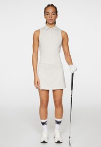 Ljusgrå ärmlös golfklänning med krage, en figursydd midja och en utsvängd kjol. Inkluderar en golfklubba och vit handske, i kombination med randiga strumpor.