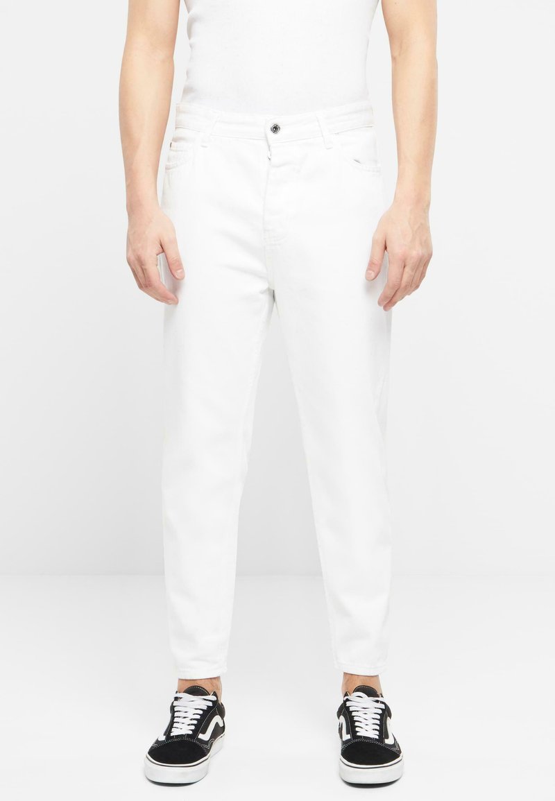 Pantalones de mezclilla blancos con corte ajustado, diseño de cinco bolsillos y cierre de un solo botón. Combinados con zapatillas en blanco y negro.