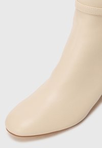 Bottines en cuir beige avec un design élégant, bout pointu, texture lisse et détails de couture subtils au niveau de la cheville.