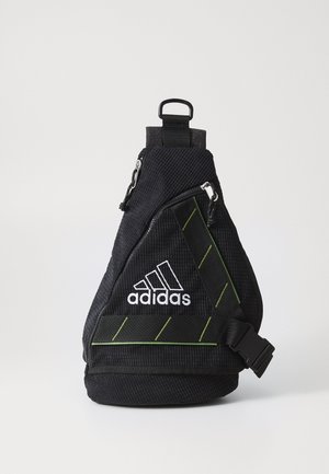 Svart stoff slingbag med teksturert overflate, hvit logo, grønne detaljer, justerbar stropp og frontlomme med glidelås. Kompakt og trekantet form.