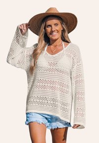 Pull crème en tricot ouvert avec des manches longues et un col large, associé à un short en denim déchiré. Le tissu présente des motifs texturés.