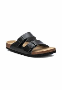 Sandalias de cuero negro con dos correas ajustables con hebillas, plantilla de corcho y suela de goma texturizada. El diseño plano permite un fácil acceso al ponerlas.