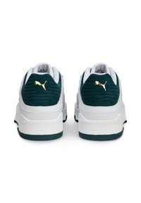 Weiße Wildleder- und Mesh-Sneaker mit grünen Akzenten, ausgestattet mit einer strukturierten Rückseite und einem goldenen Logo an der Ferse. Flache Gummisohle.
