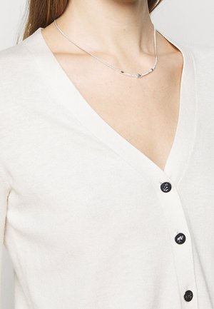 Cardigan crème avec un col en V, doté de boutons foncés sur le devant; texture en maille douce avec une silhouette ajustée.