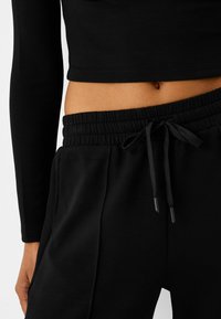 Haut court noir à manches longues associé à un pantalon de jogging noir avec cordon de serrage. Le pantalon de jogging possède une taille élastique et des poches latérales discrètes.