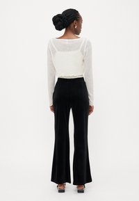 Witte cropped longsleeve top met een delicate textuur, gecombineerd met zwarte flared fluwelen broek met een elastische tailleband en elegante sandalen.