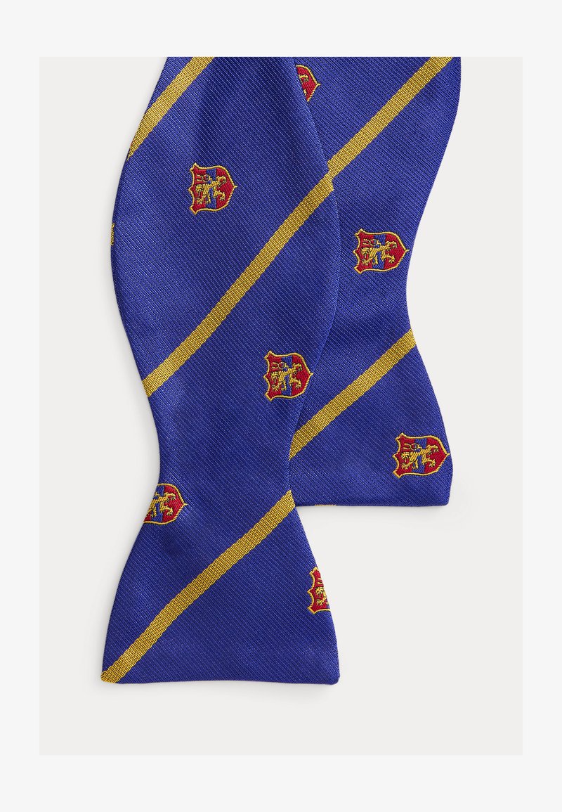 Μπλε παπιγιόν με αυτοδέσιμο, με διαγώνιες χρυσές ρίγες και μοτίβα ερυθρών, κίτρινων και μπλε εμβλημάτων σε επαναλαμβανόμενη διάταξη στο ύφασμα.