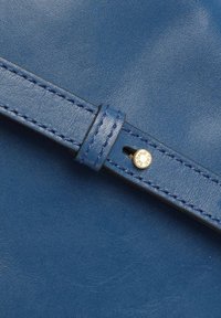 Cinturino in pelle blu con una texture liscia, caratterizzato da cuciture a contrasto e un rivetto metallico con incisione.