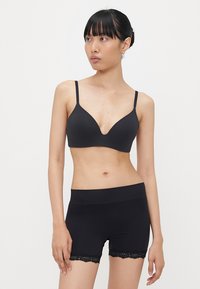 Zwarte bralette met dunne bandjes en een diepe V-halslijn, gecombineerd met hoge zwarte shorts met kantafwerking aan de zoom.