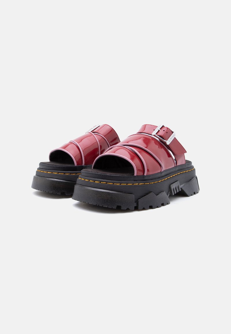 Sandali platform neri e massicci con cinturini in pelle rossa lucida e fibbie argentate su sfondo bianco.