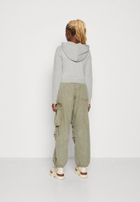 Felpa grigia tagliata con cappuccio regolabile, abbinata a pantaloni cargo larghi di colore verde oliva con tasche laterali e polsini elastici. Calzature chunky di colore crema.