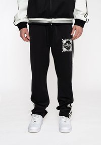 Sorte sweatpants lavet af bomuldsblanding, med en hvid grafik på venstre lår, sidelister og snor i taljen.