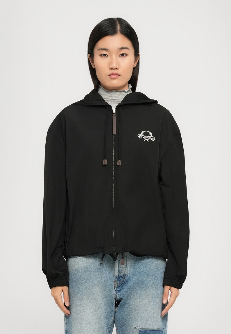 Črna zip-up jakna s kapuco, ki ima elastične manšete, zategnjen rob in belo vezeno logo na levem prsnem delu.