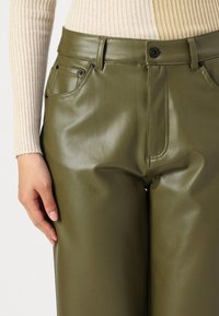 Pantalon en simili cuir vert olive présentant une texture lisse, des poches avant, des passants de ceinture et de subtils détails de couture.