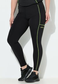 Leggings negros hechos de un material elástico con costuras de acento verdes y un bolsillo lateral con el logo "sprts".