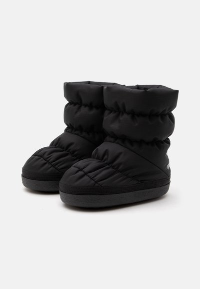 Paire de bottes d'hiver isolées noires avec des dessus matelassés et matelassés et des semelles plates en caoutchouc sur un fond clair uni.