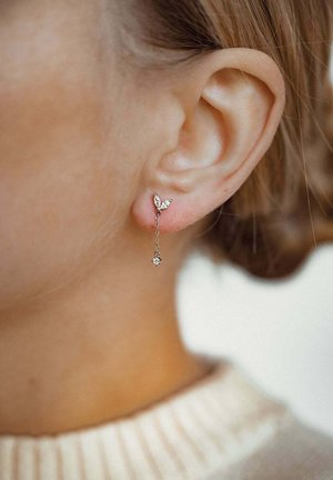 Silberne Ohrringe mit einem Schmetterlingdesign, verziert mit klaren Edelsteinen, die an einer zarten Kette mit einem kleinen Anhänger am Ende hängen.