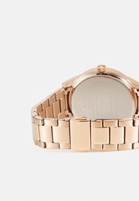 Reloj de metal en color oro rosa con un diseño de pulsera de eslabones y una caja redondeada. Presenta un fondo liso y una pequeña corona en la parte superior.