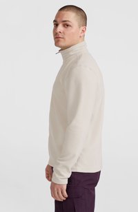 Pullover in polar beige chiaro con colletto alto e maniche lunghe. Presenta cuciture piatte e un design semplice, abbinato a pantaloni viola scuro.