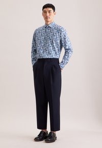 Blauw-wit bloemdessin gedrukt overhemd met lange mouwen, gecombineerd met marineblauwe hoge taille broek en zwarte veterschoenen.