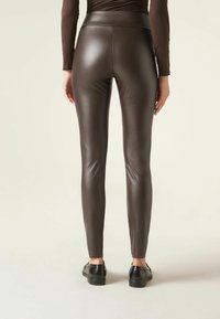 Bruine nepleer legging met een hoge tailleband, een aansluitend ontwerp en een gladde textuur, gecombineerd met zwarte schoenen.