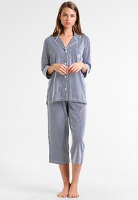 Raidoitu kaksiosainen pyjama-asuste tummansinisenä ja valkoisena. Napillinen paita pitkillä hihoilla ja lyhyet housut. Pehmeä kankaan rakenne.