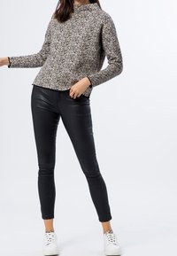 Suéter de punto en un patrón moteado, beige y negro, combinado con pantalones ajustados de piel sintética negra y zapatillas blancas.