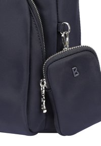 Sac à dos en tissu bleu marine avec une surface texturée, présentant des zippers argentés et une petite pochette zippée détachable avec un "B" gaufré.