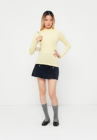 Lichtgele ribbelige longsleeve top met een gerimpelde halslijn, gecombineerd met een marineblauwe corduroy rok met twee zilveren knopen. Grijze kniehoge sokken en zwarte ballerina's.