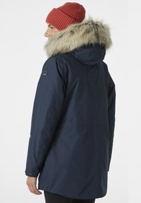 Navy blue parka with a fur-lined hood, featuring a zipper and button closure, black logo patch on shoulder, and a smooth, matte texture.