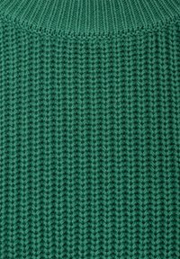 Gros plan d'un tissu tricoté vert montrant une texture côtelée verticale détaillée et un motif de points.