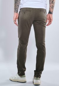 Olive green slim-fit trousers with two back pockets featuring buttons, worn with white sneakers, showcasing a smooth, textured fabric.