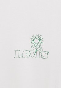 Bílá látka s vyšitým zeleným logem "Levi's" a květinovým vzorem nad ním. Jednoduché, čisté linie bez dalších vzorů.