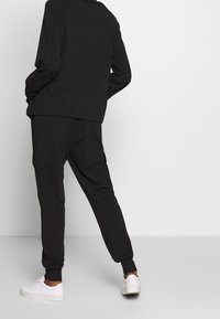 Czarna bluza z luźnym krojem i okrągłym dekoltem, w zestawie z dopasowanymi dresami z bocznymi kieszeniami. Całość dopełniają białe sneakersy.